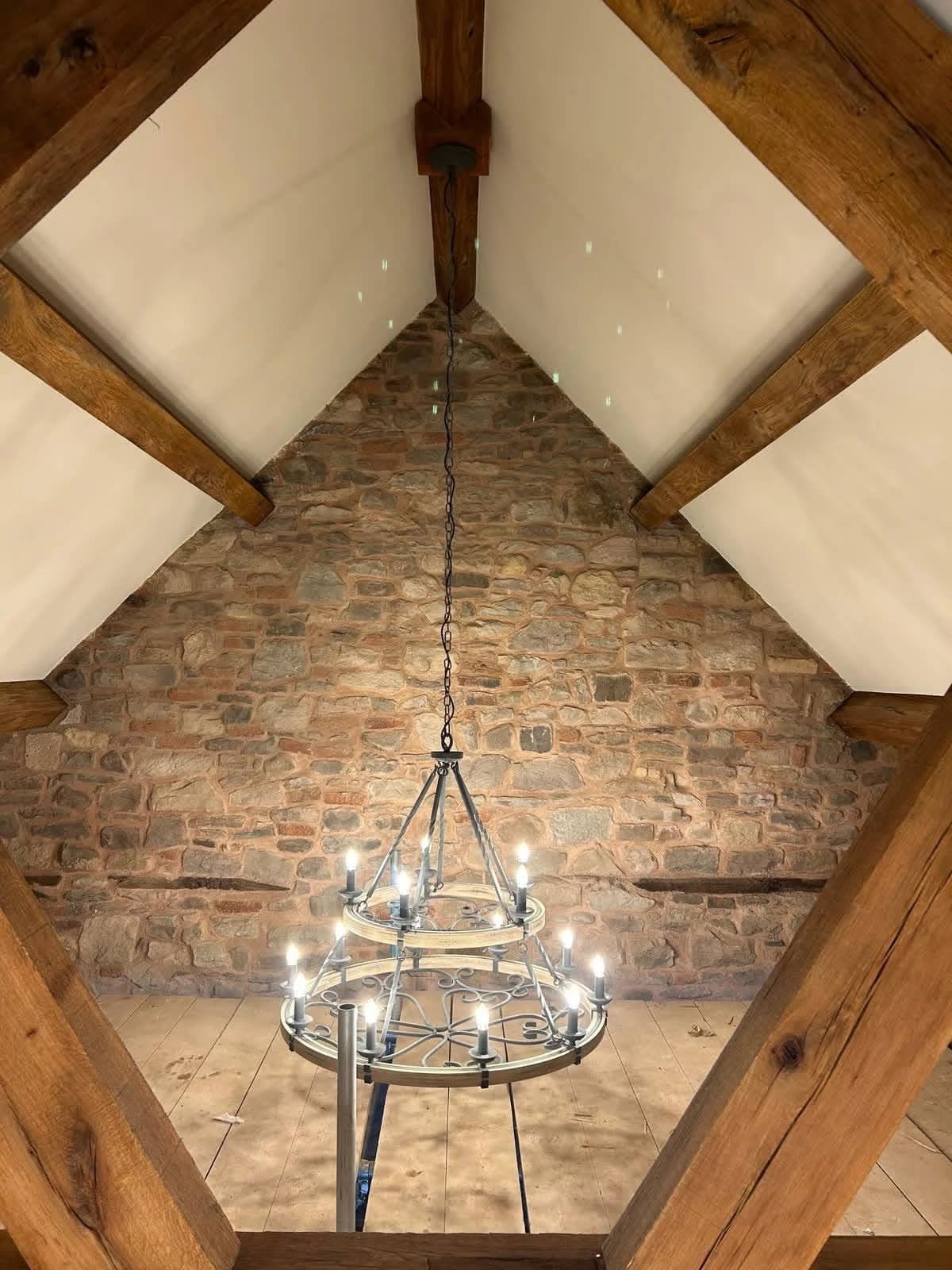 A converted barn interior by DSL Plastering, with an exposed stone gable wall, oak roof trusses and smooth plastered panels between the timbers